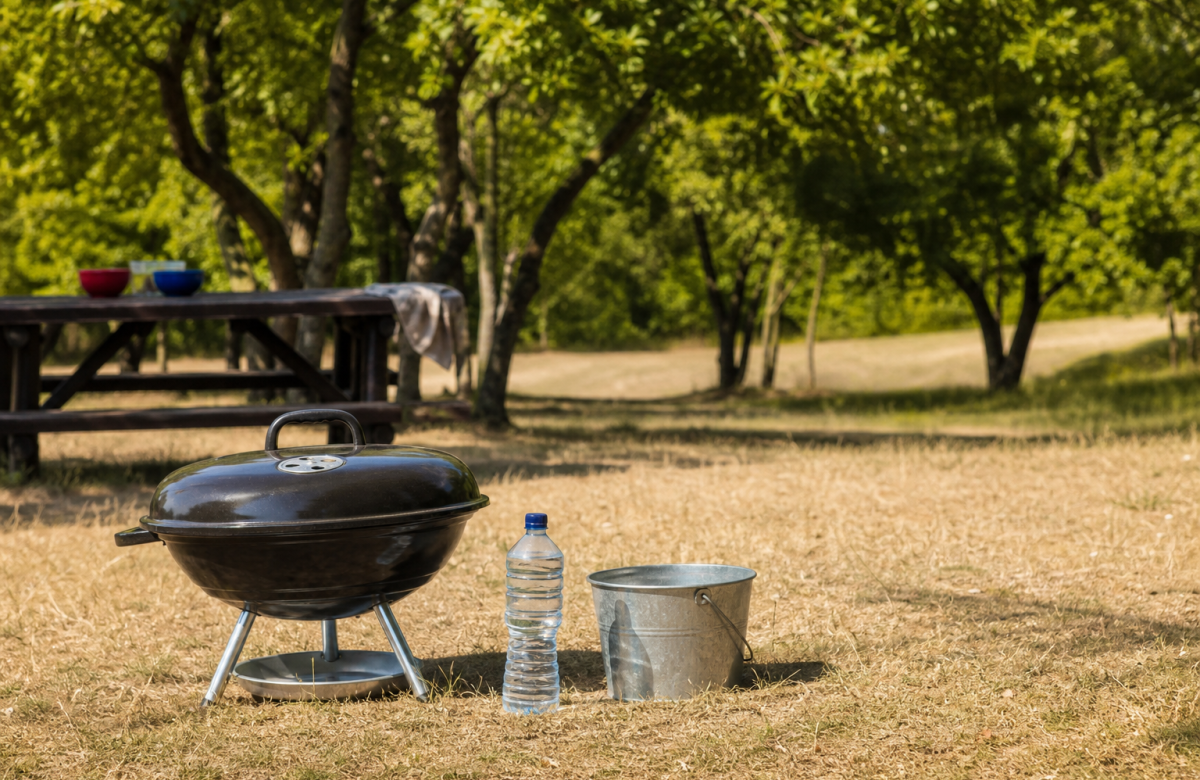 Barbecue spento con acqua e secchio in area verde generica